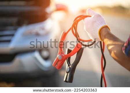 Car broken on the road. Man holding red and black battery cable for charging the car. Car Repair and maintenance concept Royalty-Free Stock Photo #2254203363