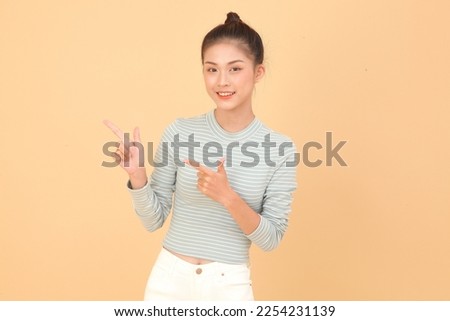 Portrait of South East Asian young, beautiful happy cheerful lady, with hand gesture pointing something, isolated on background. Concept of exciting enjoyment to show the content in the air.