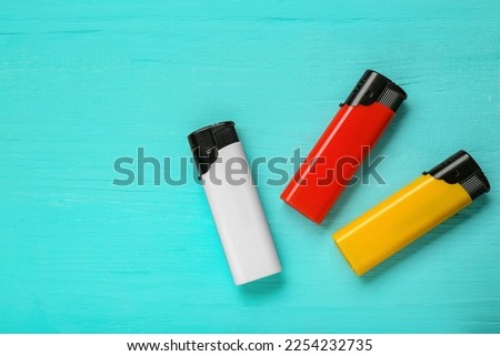 Stylish small pocket lighters on turquoise wooden background, flat lay. Space for text