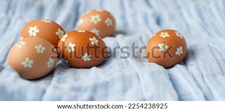 Easter eggs of natural color with painted tiny flowers on them on a blue linen fabric. Creative easy idea of decorating eggs. Neutral colors, aesthetics. Selective focus.