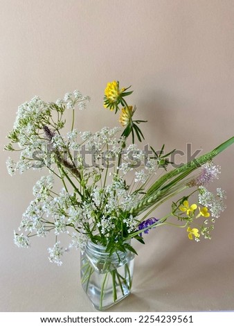 Bouquet of small wild flowers in a glass jar. Part of a bouquet with small yellow and white flowers on a beige background. Empty space for text, image or logo.