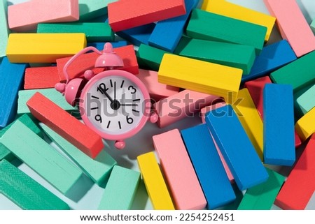 Block tower made of colourfull wooden blocks on light blue background and a clock
