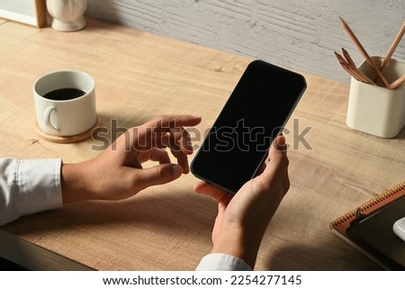 Man hand holding smart phone over wooden office desk. Close up view, blank screen for your advertise
