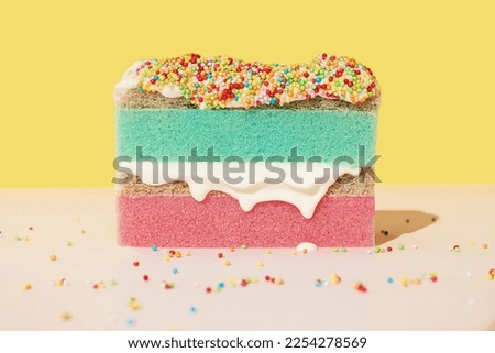 Pink kitchen cleaning sponge as a sponge cake with whipped cream and colourful sprinkles on a yellow and green background. Creative concept of holiday celebrating. Happy birthday wallpaper. Household.