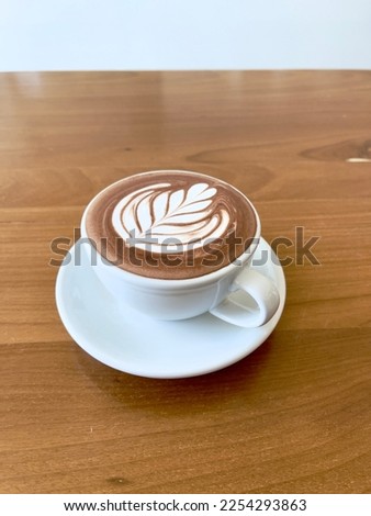 Hot cocoa with beautiful latte art, selective focus. Hot chocolate with white creamy leaves pattern in white ceramic cup.