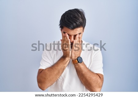 Hispanic man standing over blue background rubbing eyes for fatigue and headache, sleepy and tired expression. vision problem 