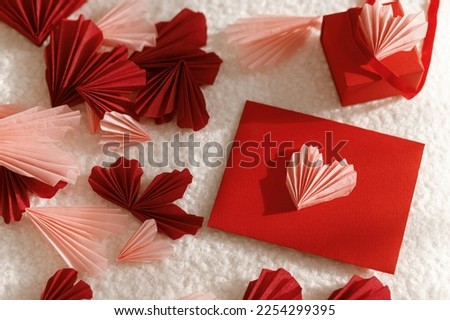 Happy Valentine's day! Stylish red envelope with pink hearts and gift on cozy soft fabric in sunlight. Modern valentine card with heart cutouts. Love letter. Creative composition