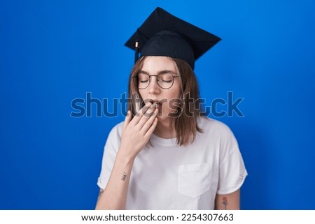 Blonde caucasian woman wearing graduation cap bored yawning tired covering mouth with hand. restless and sleepiness. 