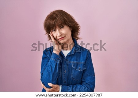 Middle age woman standing over pink background thinking looking tired and bored with depression problems with crossed arms. 