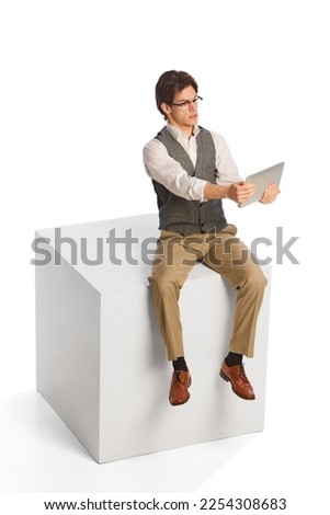 Young thoughtful business man wearing modern office style clothes sitting and using digital tablet isolated on white background. Business, work, career, education concept. Royalty-Free Stock Photo #2254308683