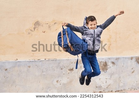 Blond child holding backpack jumping at street