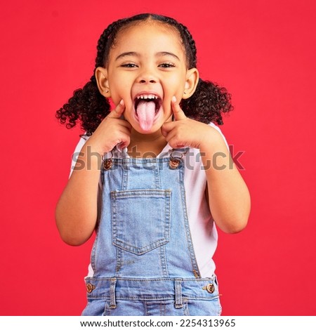 Little girl, portrait and tongue out on isolated red background in goofy, silly games and playful facial expression. Happy, kid and child with funny face in comic emoji, charades and studio activity Royalty-Free Stock Photo #2254313965