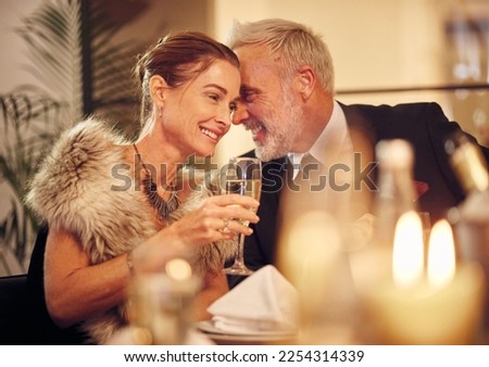 Woman, man and whisper at dinner, party or restaurant for celebration in night with smile, happy and gossip. New year, fine dining or gala event with champagne, conversation and romantic secret love Royalty-Free Stock Photo #2254314339