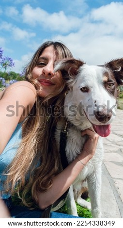 Vertical selfie portrait for social networks of young latin woman sitting in the park with her pet smiling and looking at the camera