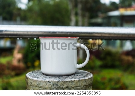Enamel mug standing on the top of a marble fence at a park with out of focus park area as the background, enamel mug mockup image