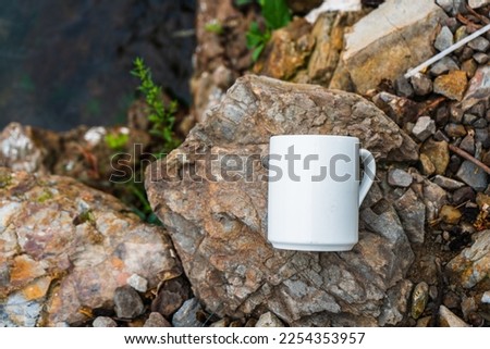 A Coffee mug laying out on the top of some rocks that covered with moss while the water keep splashing over it, coffee mug mockup image