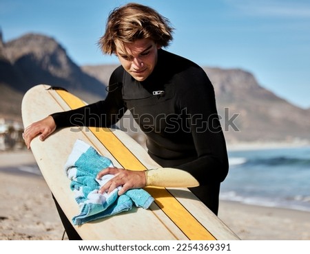 Surfing, man with surfboard on beach with fitness and travel, cleaning board and surf maintenance with extreme sport outdoor. Ocean. nature and workout, young surfer lifestyle and sports motivation