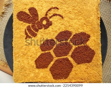 honey cake with a picture of a bee and a honeycomb on a dark gray plate