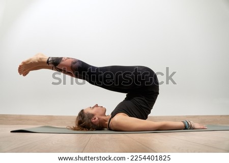 Young and sporty girl doing exercise on gray mat. Confident beautiful woman does yoga exercises in a modern sport center. Health concept. Purposeful girl trying to perform a complex exercise.