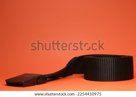Black men's belt made of nylon or canvas material on orange background isolated
