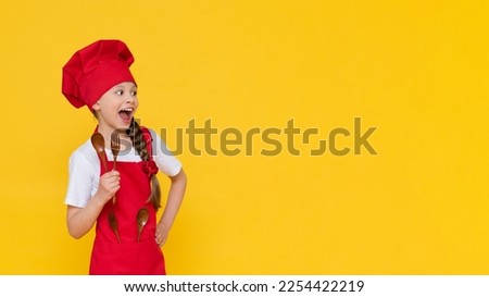 A little girl in a cook's costume, a baby cook breakfast in a chef's costume. The concept of cooking lunch, a girl cook on a yellow isolated background with copy space.