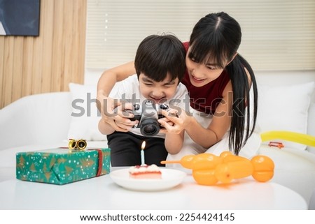 Asian young mother  teaching her son to take a photo of cake. Happy birthday kid how to record and use video camera.
