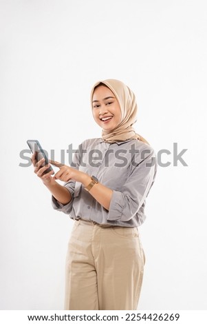 a young woman with hijab standing with smile and pointing on her phone with the white background