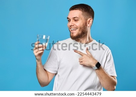 happy handsome man in white t-shirt showing drinking glass of water Royalty-Free Stock Photo #2254443479