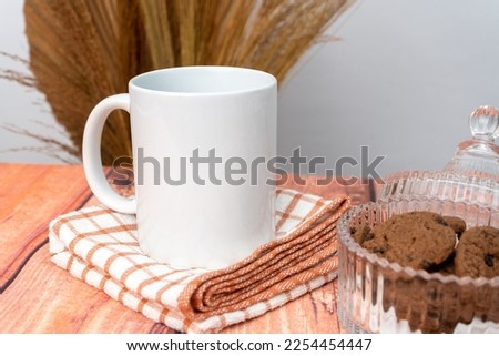 A white blank coffee mug on the top of a hand cloth with some crackers arranged beside it, coffee mug mockup image
