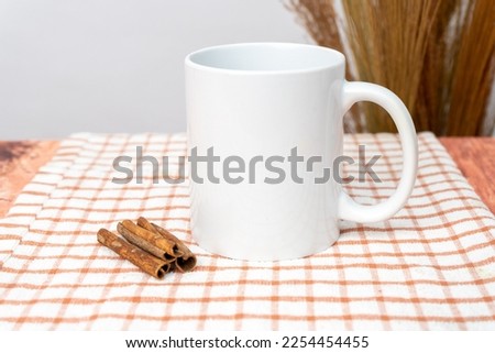 A white blank coffee mug on the top of a hand cloth with some cinnamon decorated around it, coffee mug mockup image