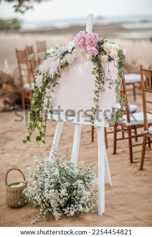 White welcome board sign with a beautiful flower decoration, standing in front of wedding entrance on the beach