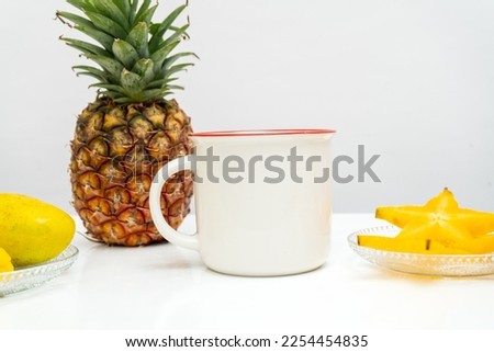 A white blank enamel mug standing out on a white table with some fresh fruit decorated around it, enamel mug mockup image