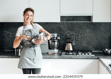 female cook stands in the kitchen by the food processor and with a metal bowl Royalty-Free Stock Photo #2254459379