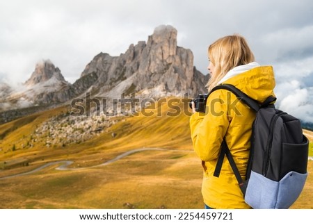 Professional photographer in yellow sport jacket takes pictures of Passo Giau pass using camera. Woman with backpack enjoys activity in Italian Alps 