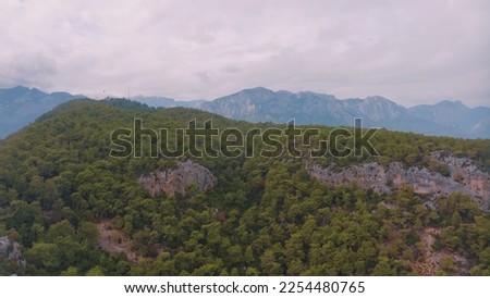 Cloudy weather. Aerial view of a rocky hill. Green trees. Human and nature. Mountain landscape. High quality photo