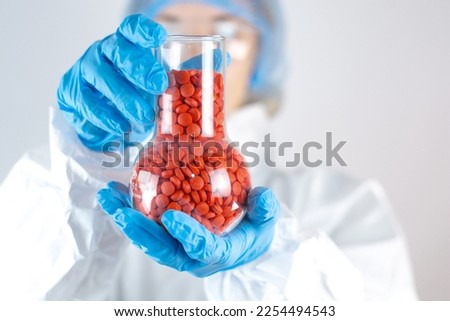 Female doctor in protective glasses and latex blue gloves on a white background with a jar of red pills Laboratory Pharmacy Medical