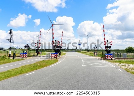 Level Crossing with Signals and Warning Signs along both a road and a bicycle lane in the countryside of Netherlands. A eind farm is in background.