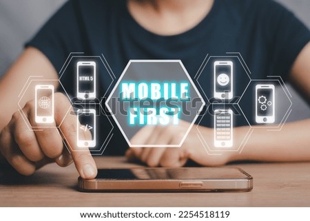 Mobile first concept, Person hand using smart phone with mobile first icon on virtual screen, Digital marketing, office desk. Royalty-Free Stock Photo #2254518119