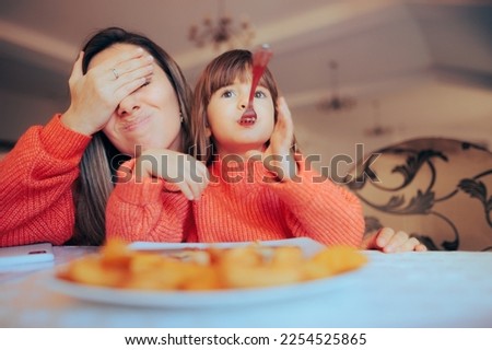 
Funny Playful Girl Eating Awkwardly Exasperating her Mom
Naughty child forgetting about table manners embarrassing her mother 
