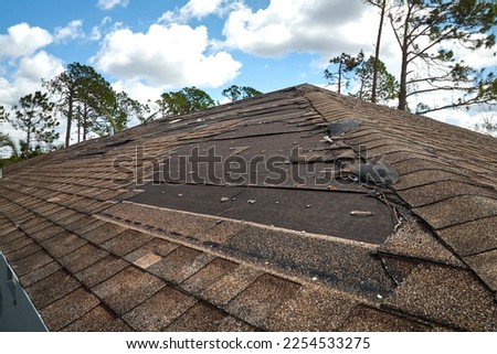 Wind damaged house roof with missing asphalt shingles after hurricane Ian in Florida. Repair of home rooftop concept Royalty-Free Stock Photo #2254533275
