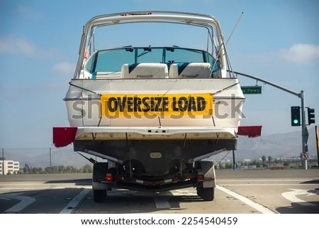 A large white motor boat being hauled on a trailer with a yellow sign stating Oversize Load Royalty-Free Stock Photo #2254540459