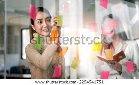 Young  businesswoman creative team using post it notes in glass wall to writing strategy business plan to development grow to success. Royalty-Free Stock Photo #2254541751