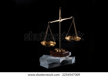 Golden scales and a large stack of 100 American dollars bills on a black background