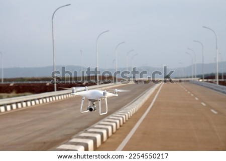 quadcopter drone with digital camera flying over road divider with empty street background.