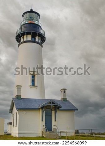 A tall white lighthouse with a small house against a sky with gray storm clouds. Mystical picture. Danger, storm, navigation, history, travel destinations, romance.