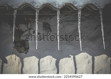 Close up icicles hanging from ruined house roof concept photo. Ice dams in winter. Front view photography with blurred background. High quality picture for wallpaper, travel blog, magazine, article