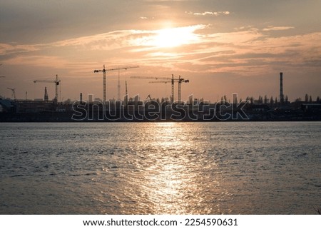 Abandoned construction cranes landscape photo. Beautiful nature scenery photography with sun behind clouds, water on background. High quality picture for wallpaper, travel blog, magazine, article