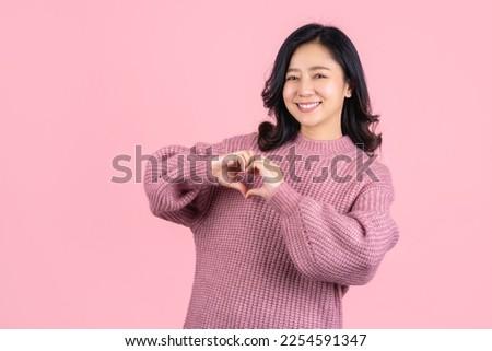 Cute asian woman showing heart shape with hands isolated on pink pastel background. Love and care people concept.