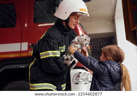 Giving scottish fold cat to the owner. Firefighter woman in uniform is with a little girl.