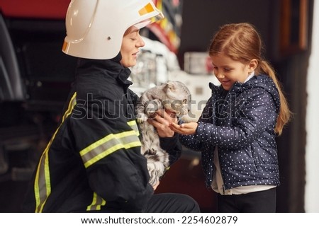 Rescued scottish fold cat. Firefighter woman in uniform is with a little girl.